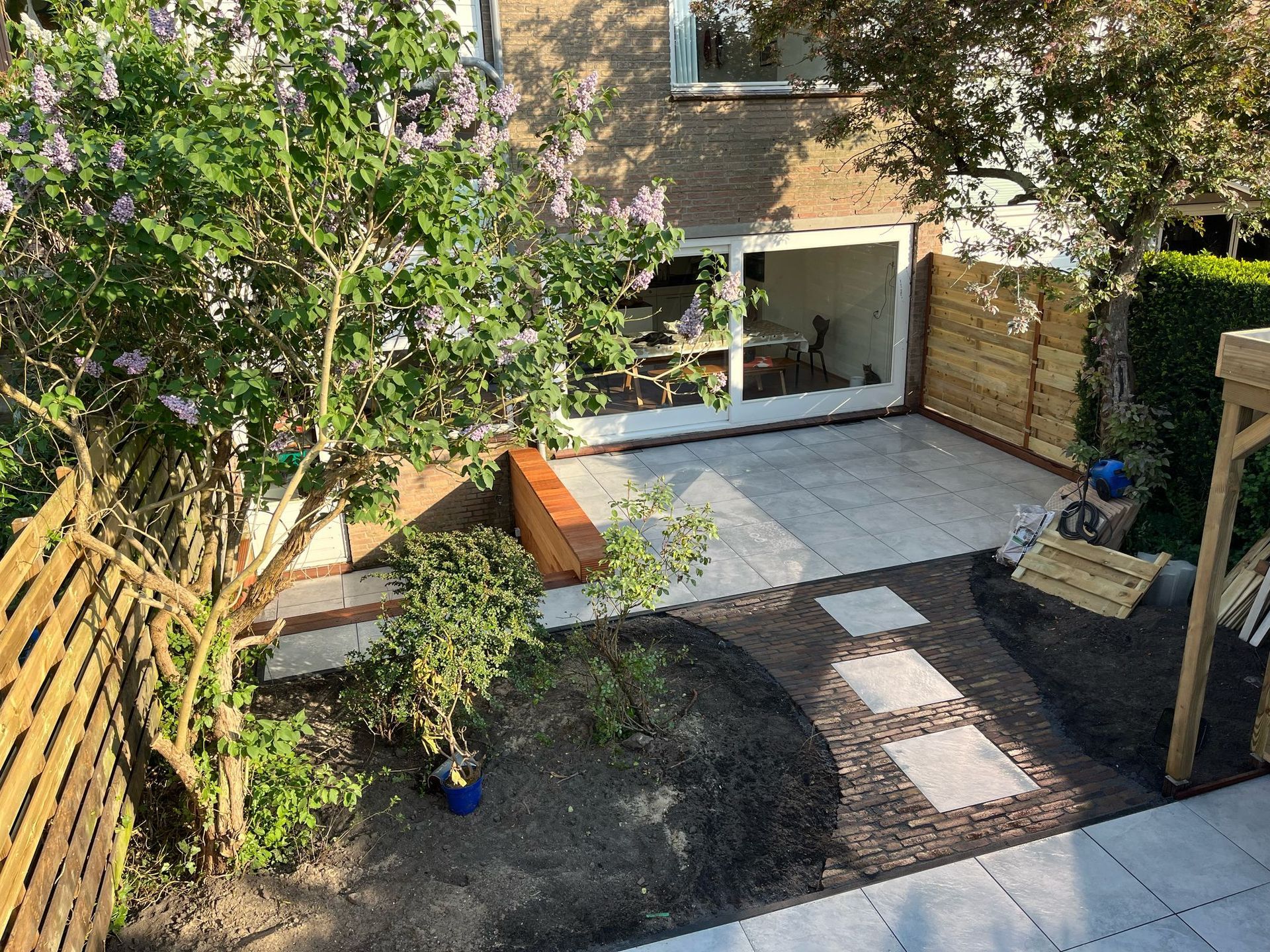 Terras in de achtertuin met stenen pad, groen en houten schutting.