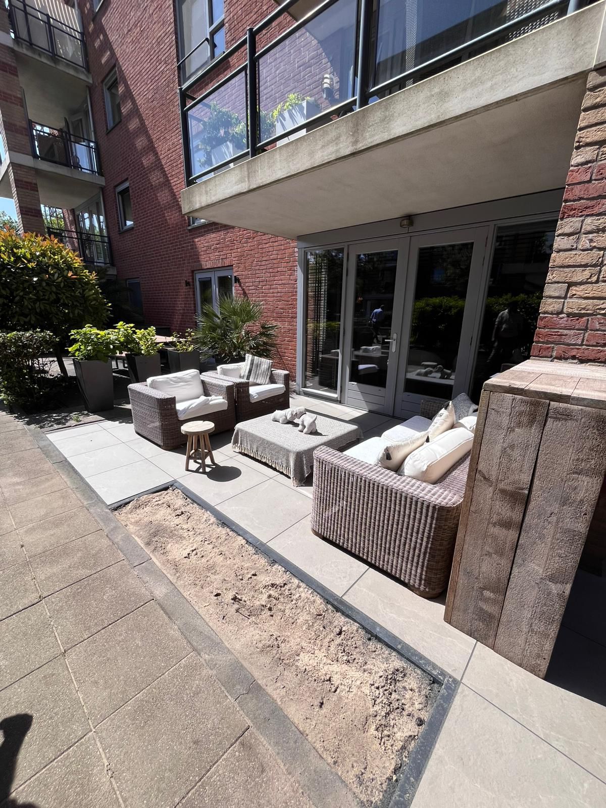 Terras met rieten meubels, glazen deuren en een bakstenen gebouw.