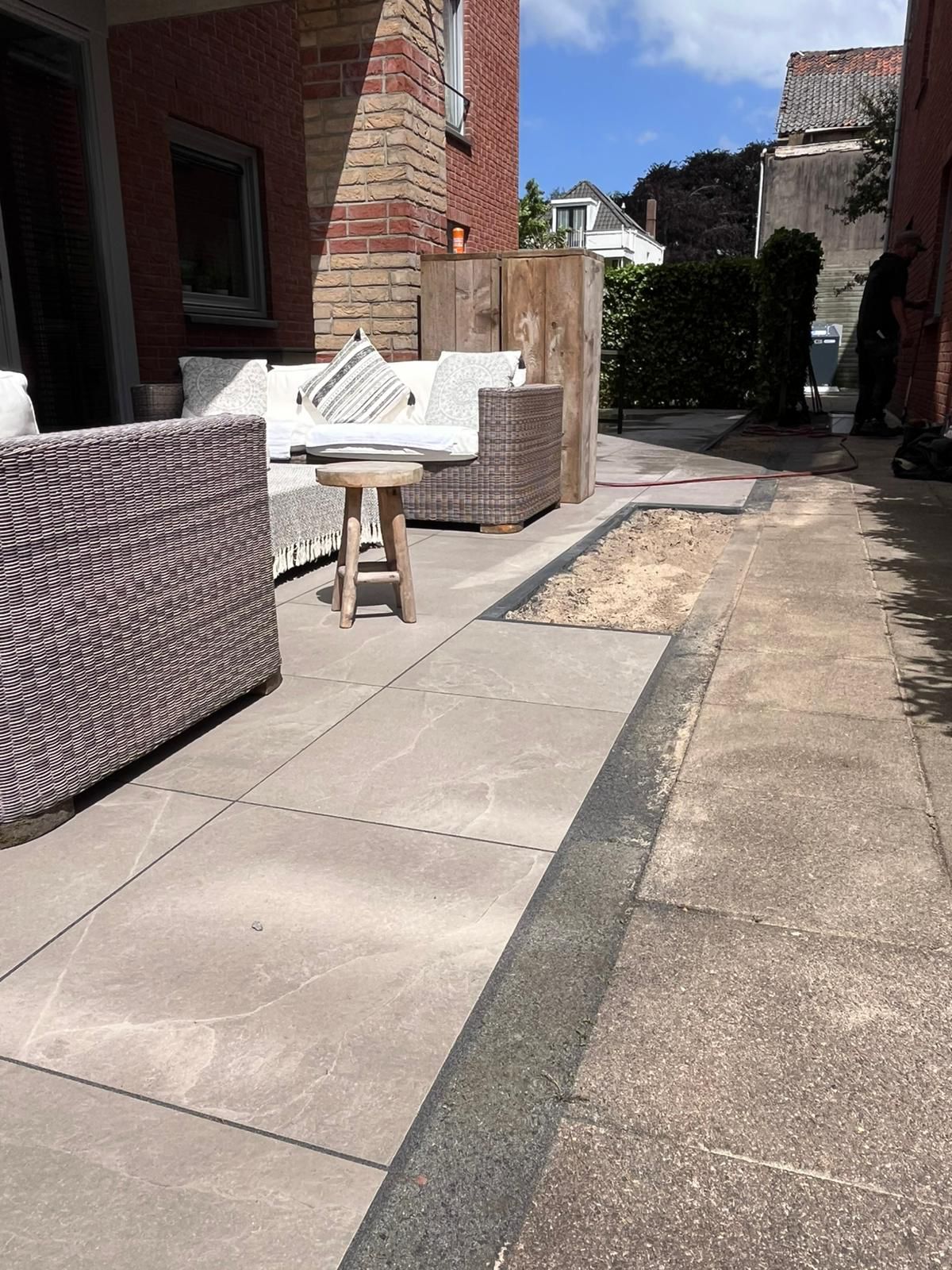 Terras met zitgelegenheid, een kleine tafel en een grindgedeelte. Op de achtergrond een bakstenen gebouw en struiken.