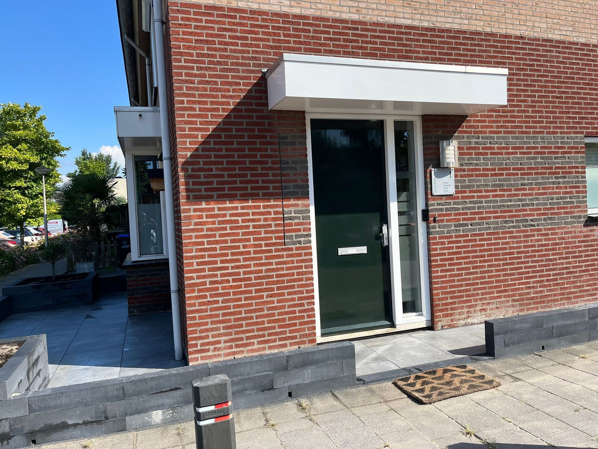 Een rood bakstenen gebouw met een donkergroene deur onder een witte luifel. Een trede leidt naar de ingang.