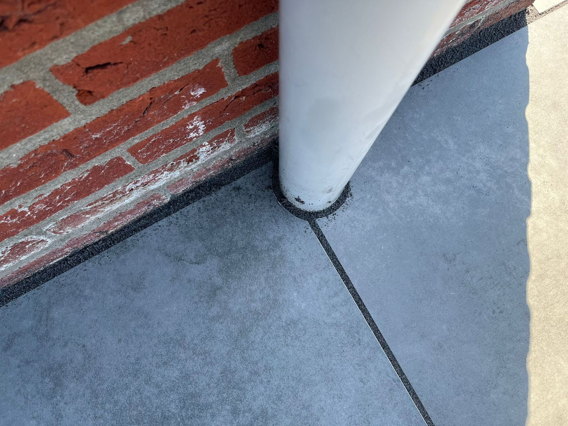 Witte buis grenst aan bakstenen muur en grijs oppervlak met donkere lijnen.
