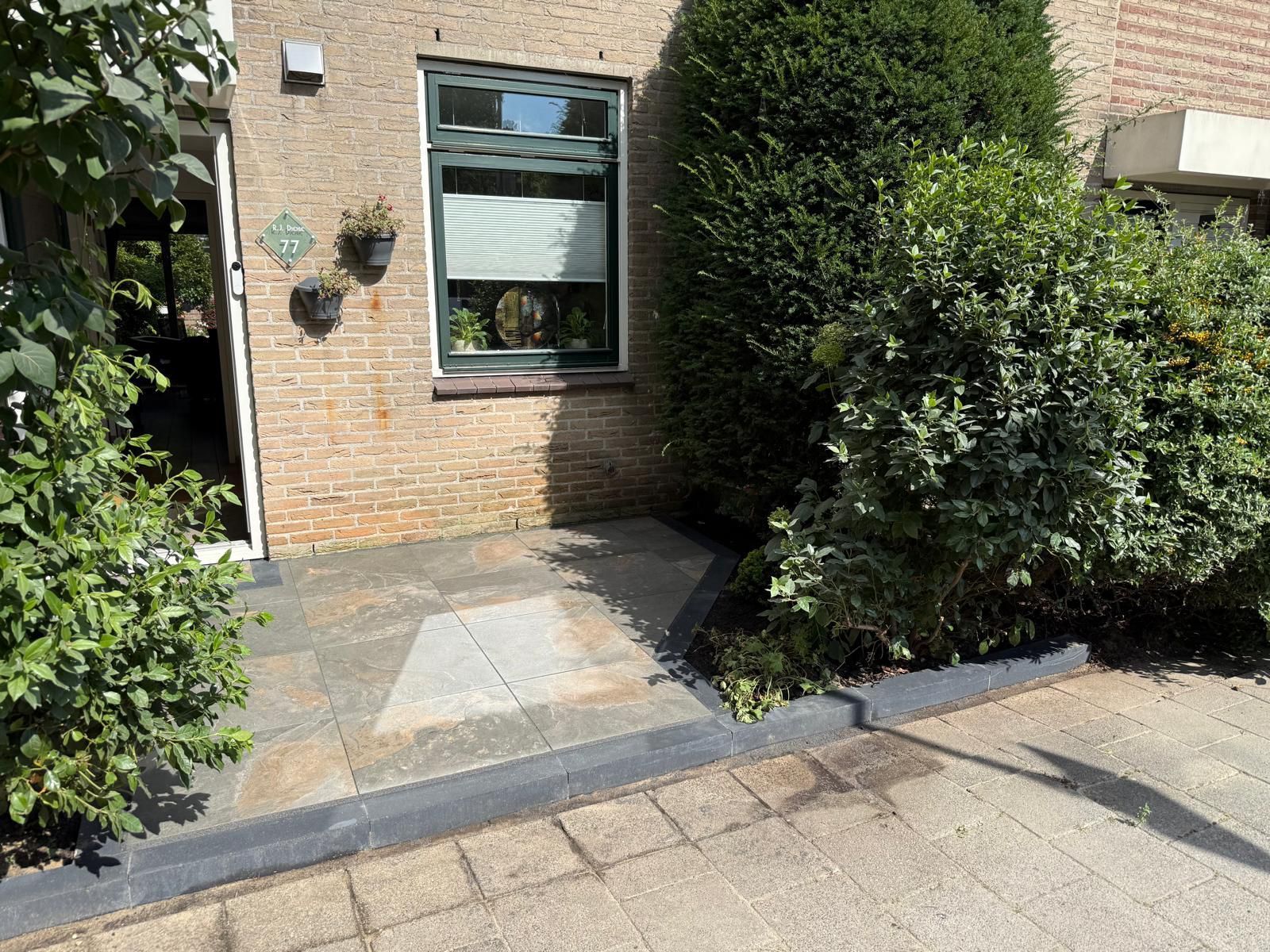 Ingang van een bakstenen gebouw met een looppad, struiken en een raam.