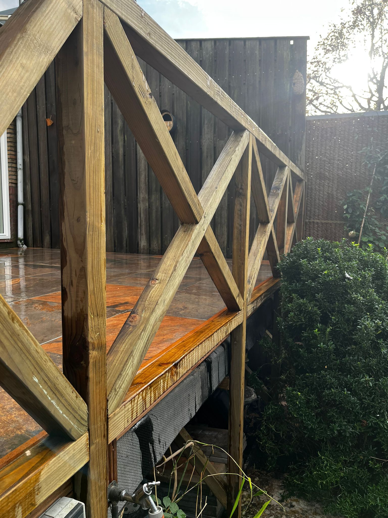 Houten balustrade met schuine dwarsbalken; regen zichtbaar.