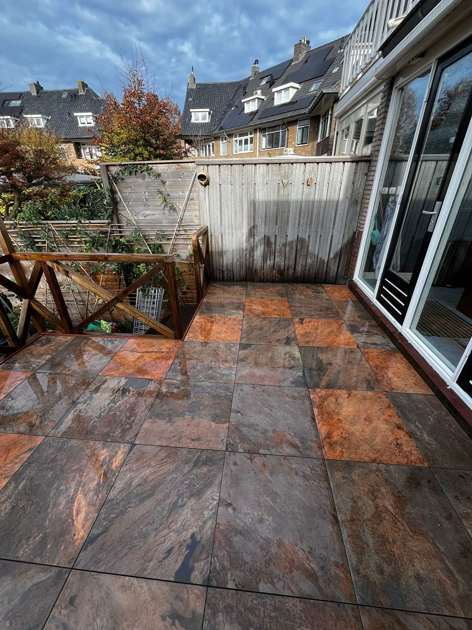 Terras met kleurrijke tegels, houten schutting en glazen deuren, woonomgeving onder een bewolkte hemel.