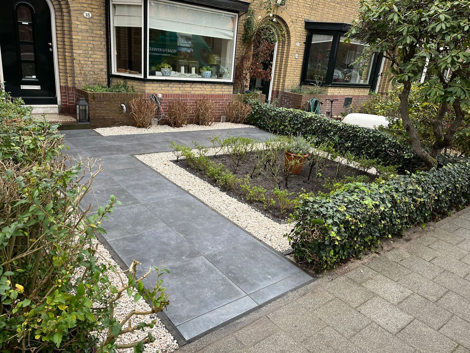 Voortuin met bestraat pad en verhoogde bloembedden.