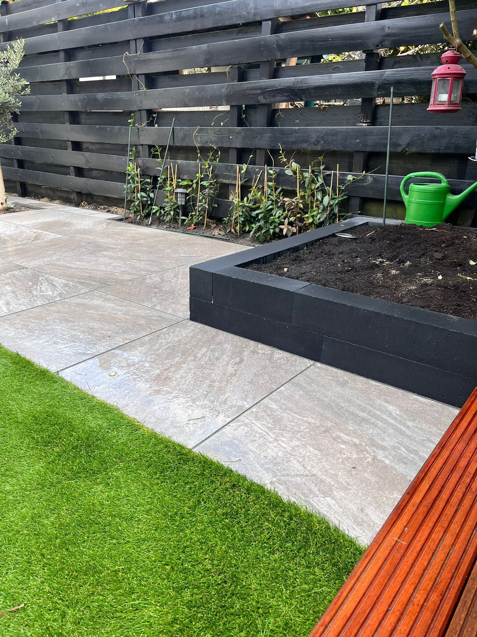 Een tuinscène met een zwart hek, een verhoogd bloembed en een groen gazon.