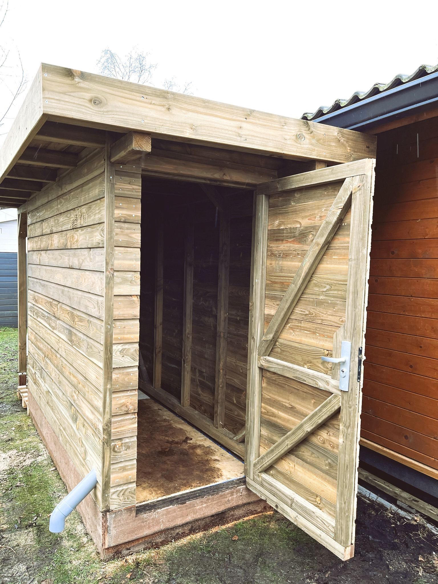 Houten schuur met open deur, grijze gevelbekleding en een dakgoot, buiten.