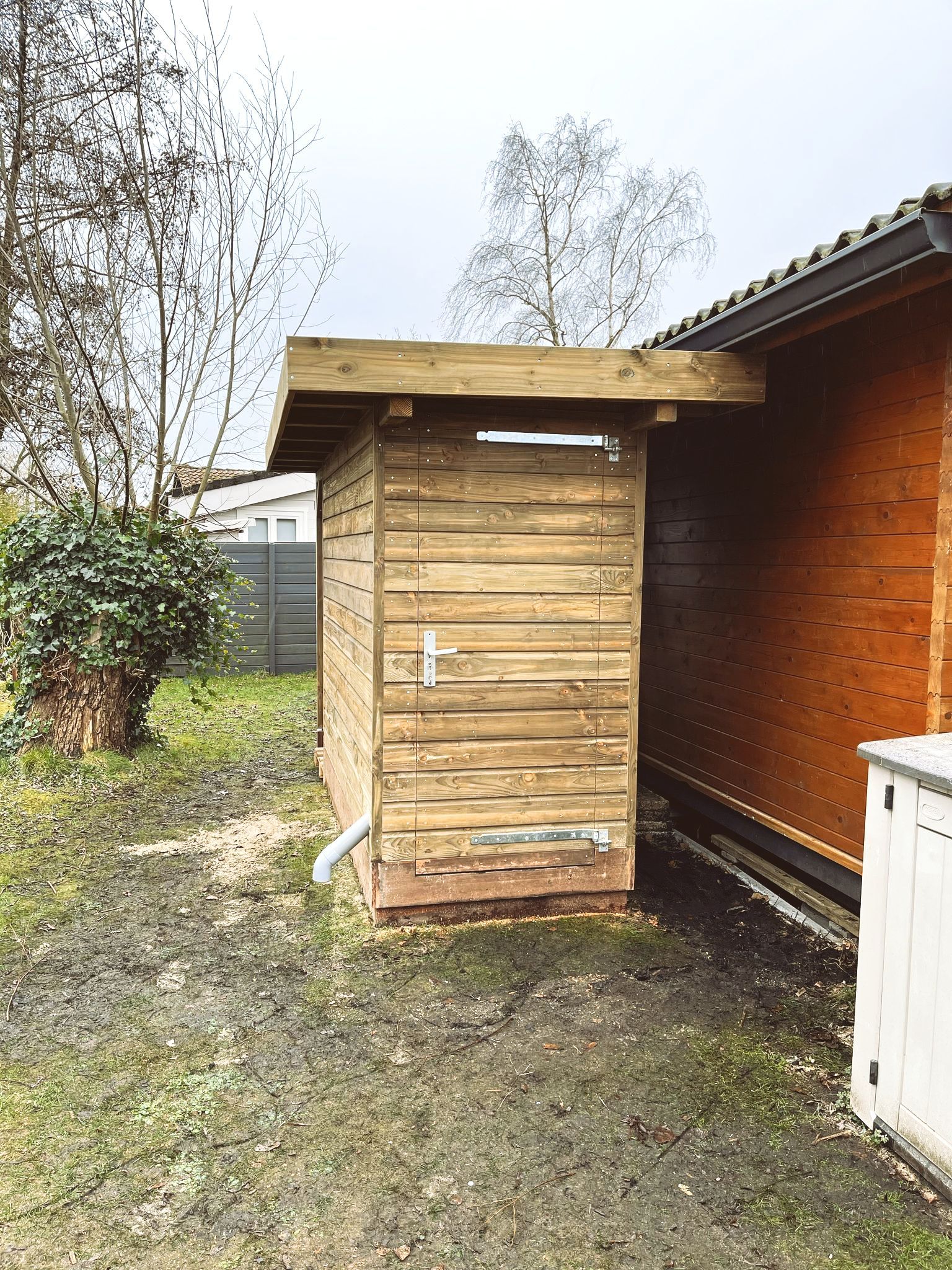 Houten schuur met een overstekend dak naast een gebouw met houten lambrisering, in een buitenomgeving.