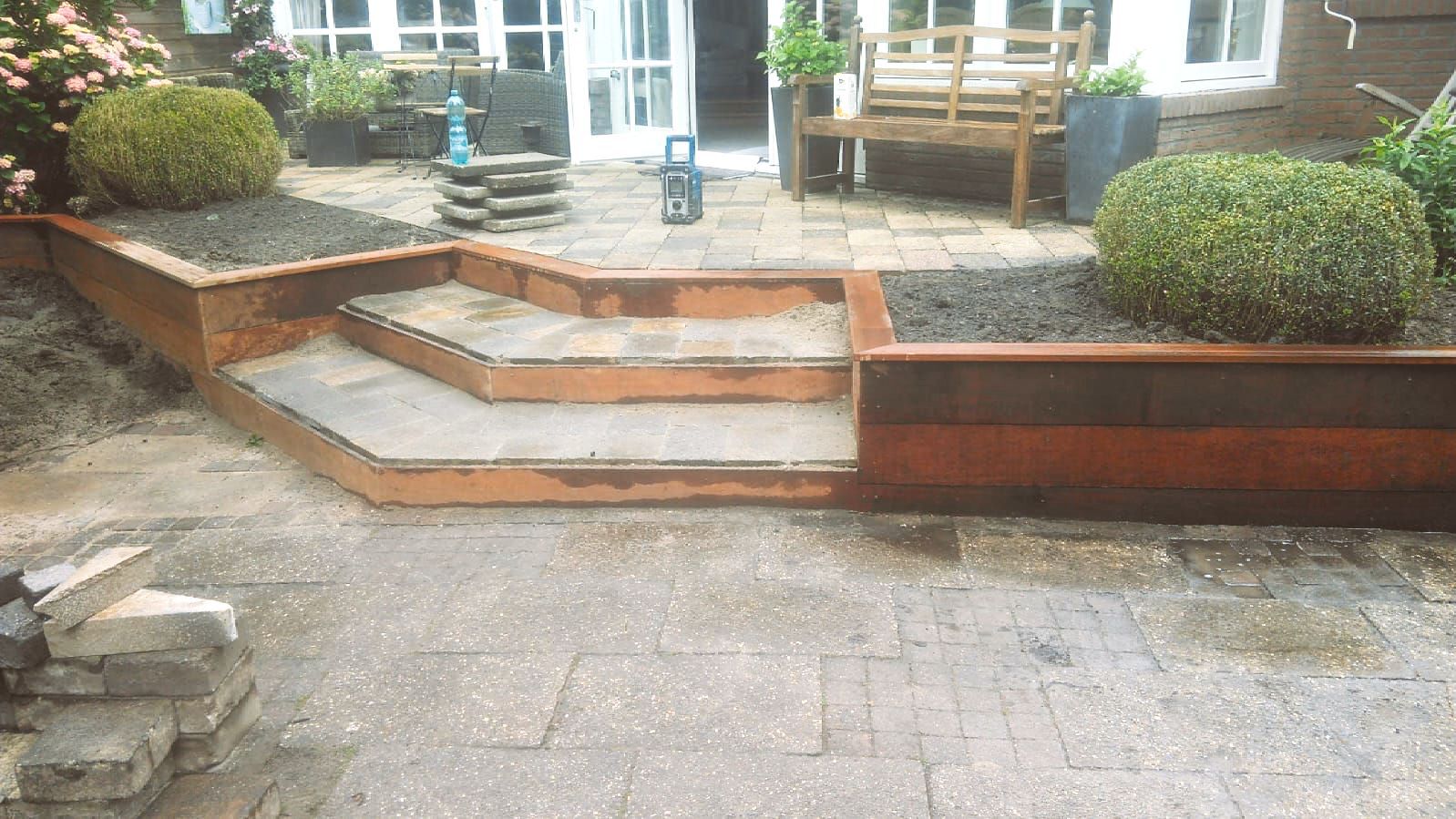 Buitenpatio met verhoogde bloembedden en een trap die naar de ingang van het huis leidt.