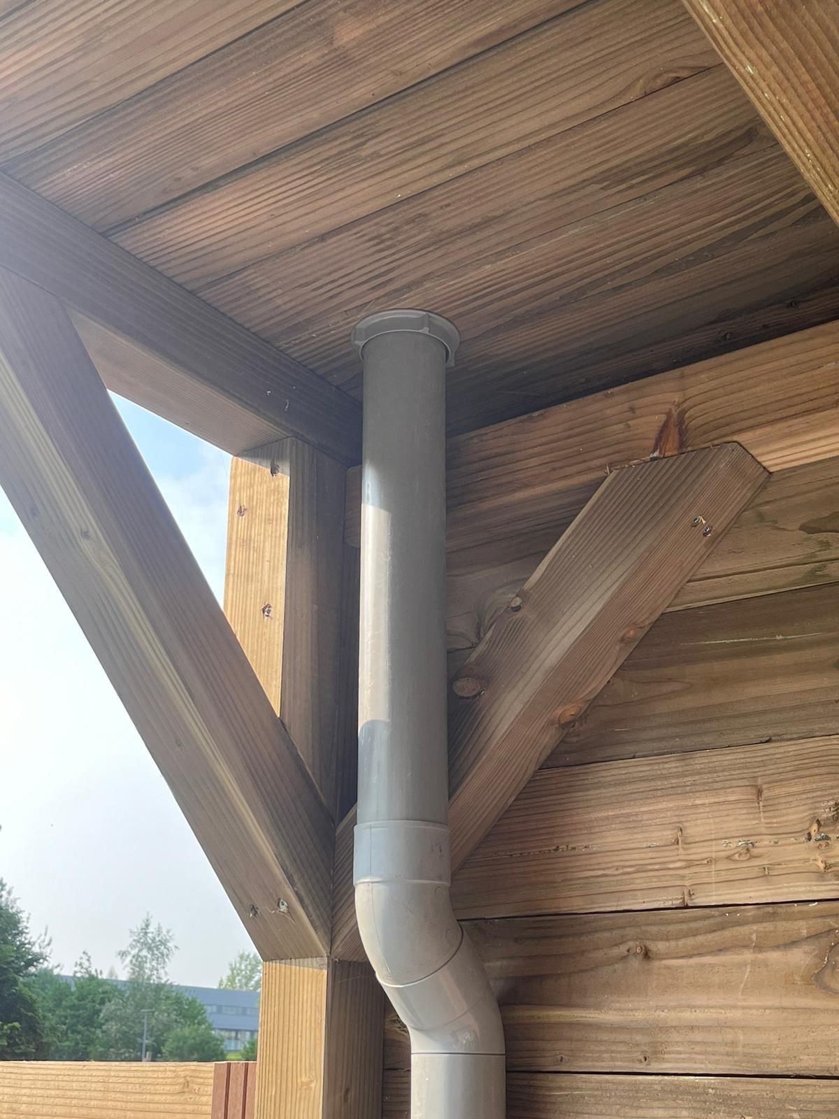 Grijze buis die door het dak van een houten constructie steekt.
