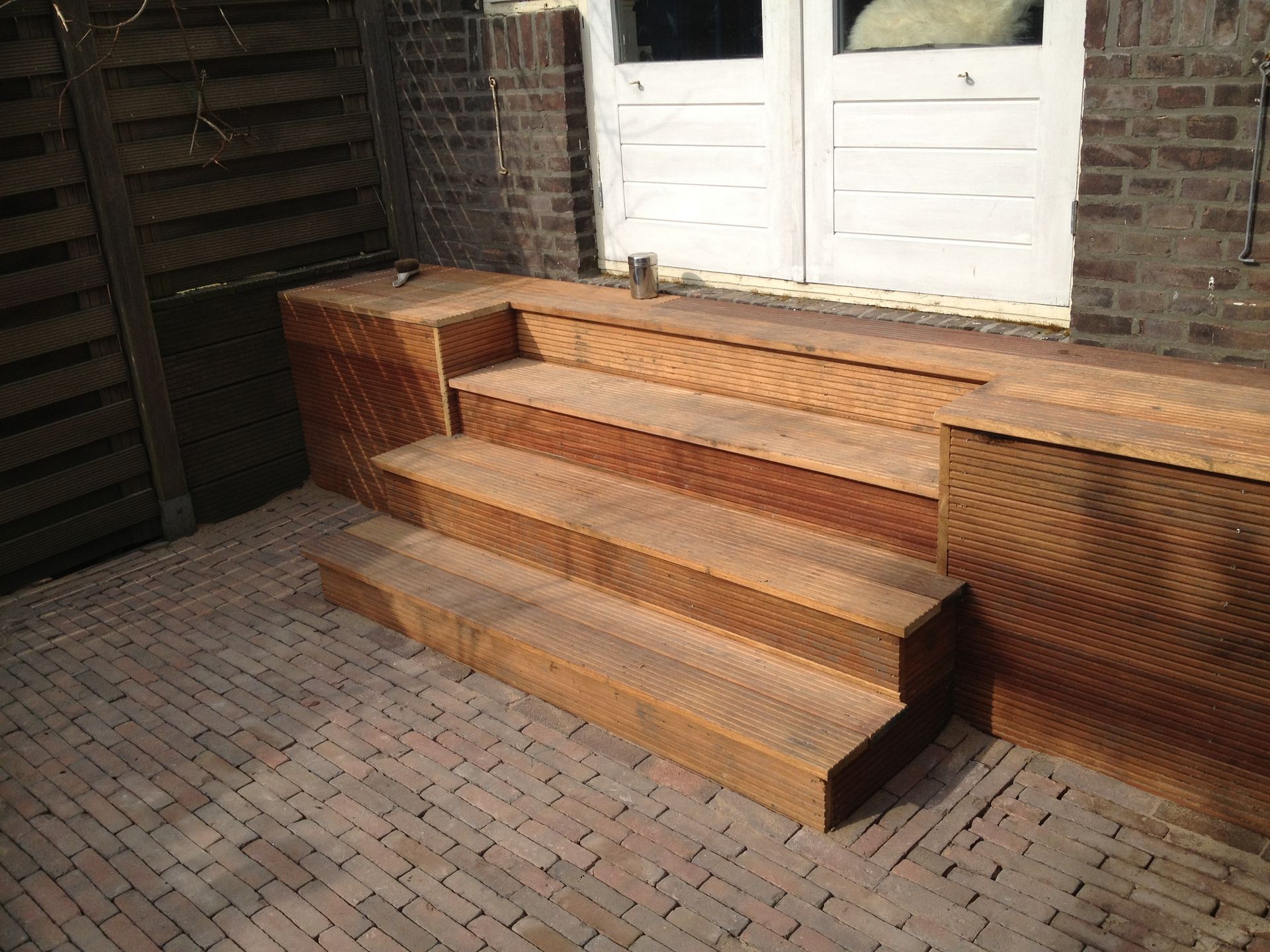 Houten treden leiden naar een witte deur, gelegen op een stenen terras.