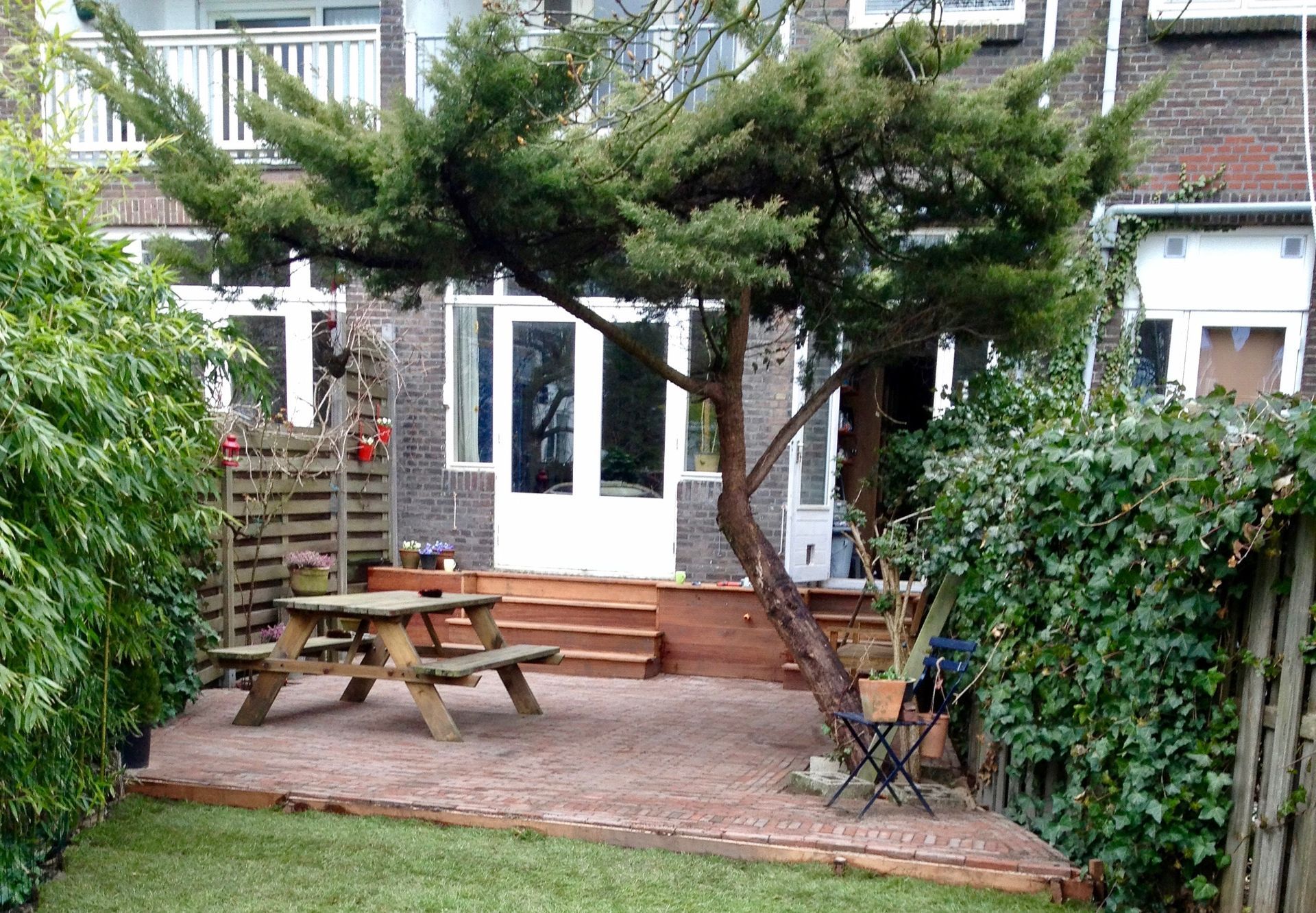 Een kleine achtertuin met een picknicktafel, een boom en een deur die naar een huis leidt.