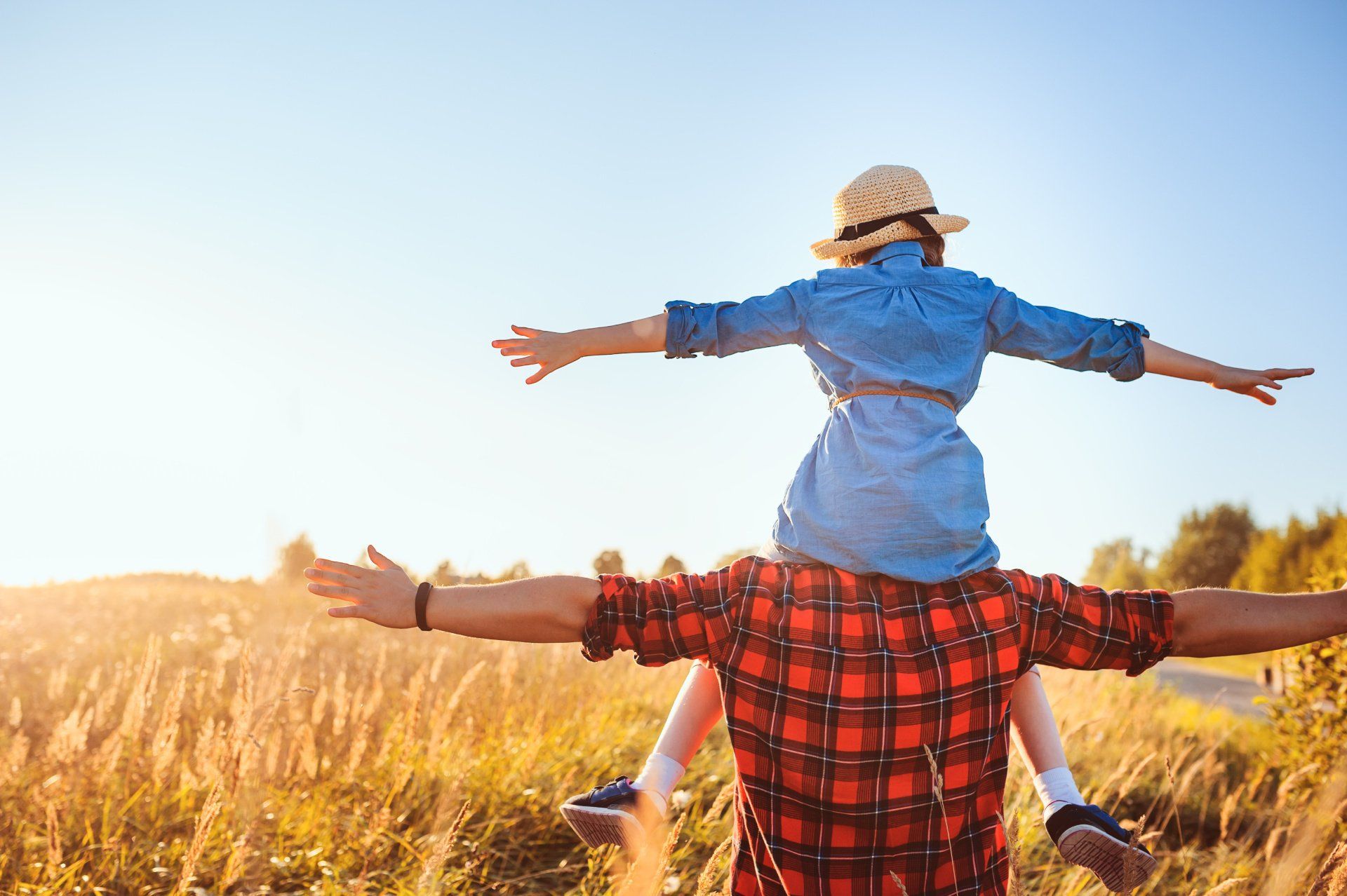 Daughter sitting on dad's shoulders with arms spread in a field
