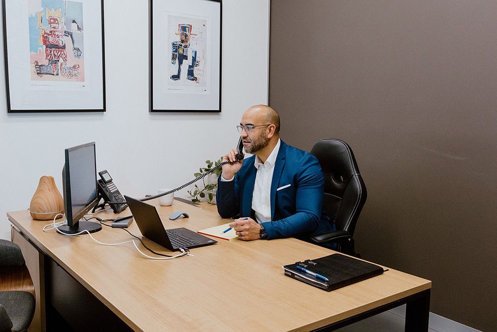 A Man Is Sitting At A Desk Talking On A Tele Phone — David Tamanika Solicitors in Bacchus Marsh, VIC