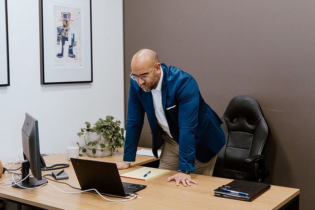 A Man In A Blue Jacket Is Standing In Front Of A Laptop Computer — David Tamanika Solicitors in Ballarat Central, VIC