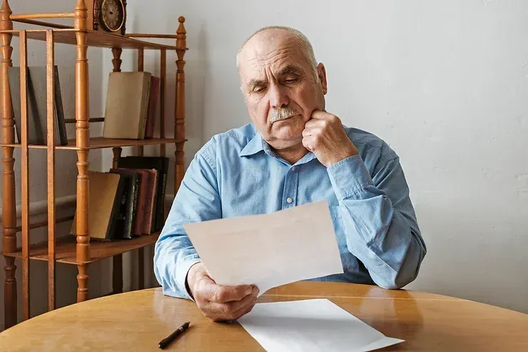An Elderly Man Is At A Table Reading A Piece Of Paper — David Tamanika Solicitors in Ballarat, VIC