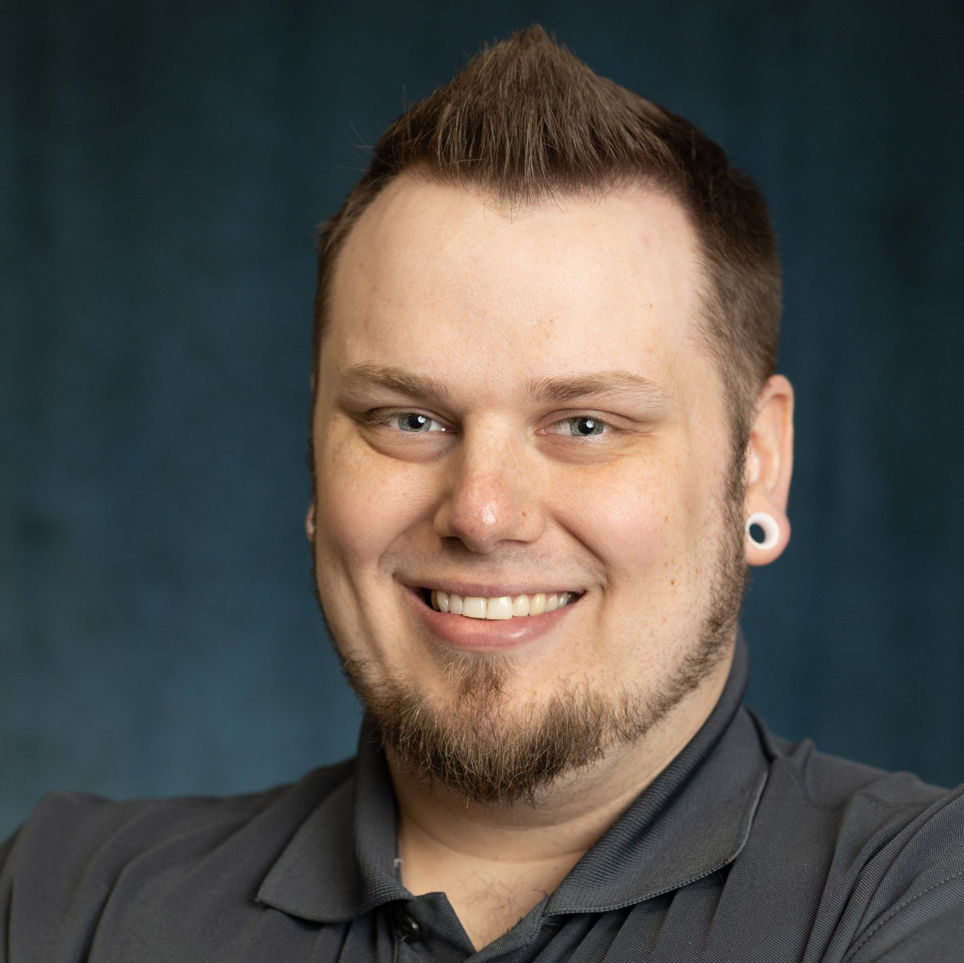 A man with a beard and ear plugs is smiling for the camera