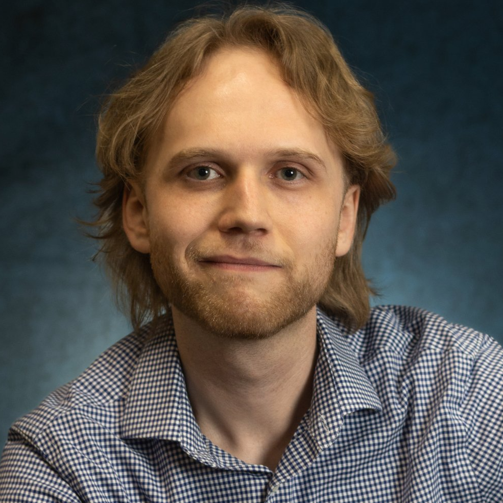 A man with a beard is wearing a plaid shirt and smiling for the camera.