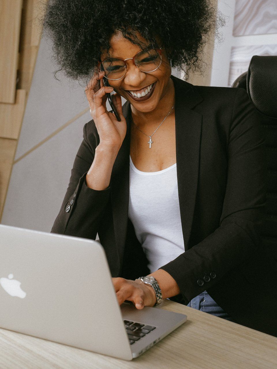A woman is talking on a cell phone while using a laptop computer.