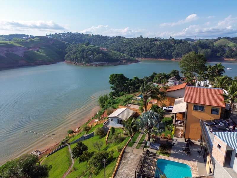 Casas com telhados alaranjados ao lado de um lago, com colinas verdejantes ao fundo.