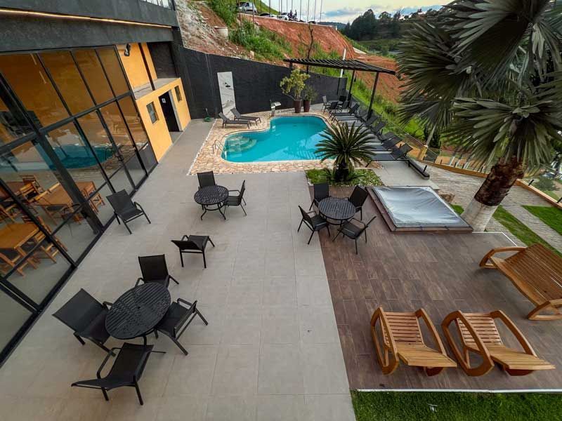 Pátio com piscina, mesas, cadeiras e jacuzzi perto de um edifício e de uma encosta.