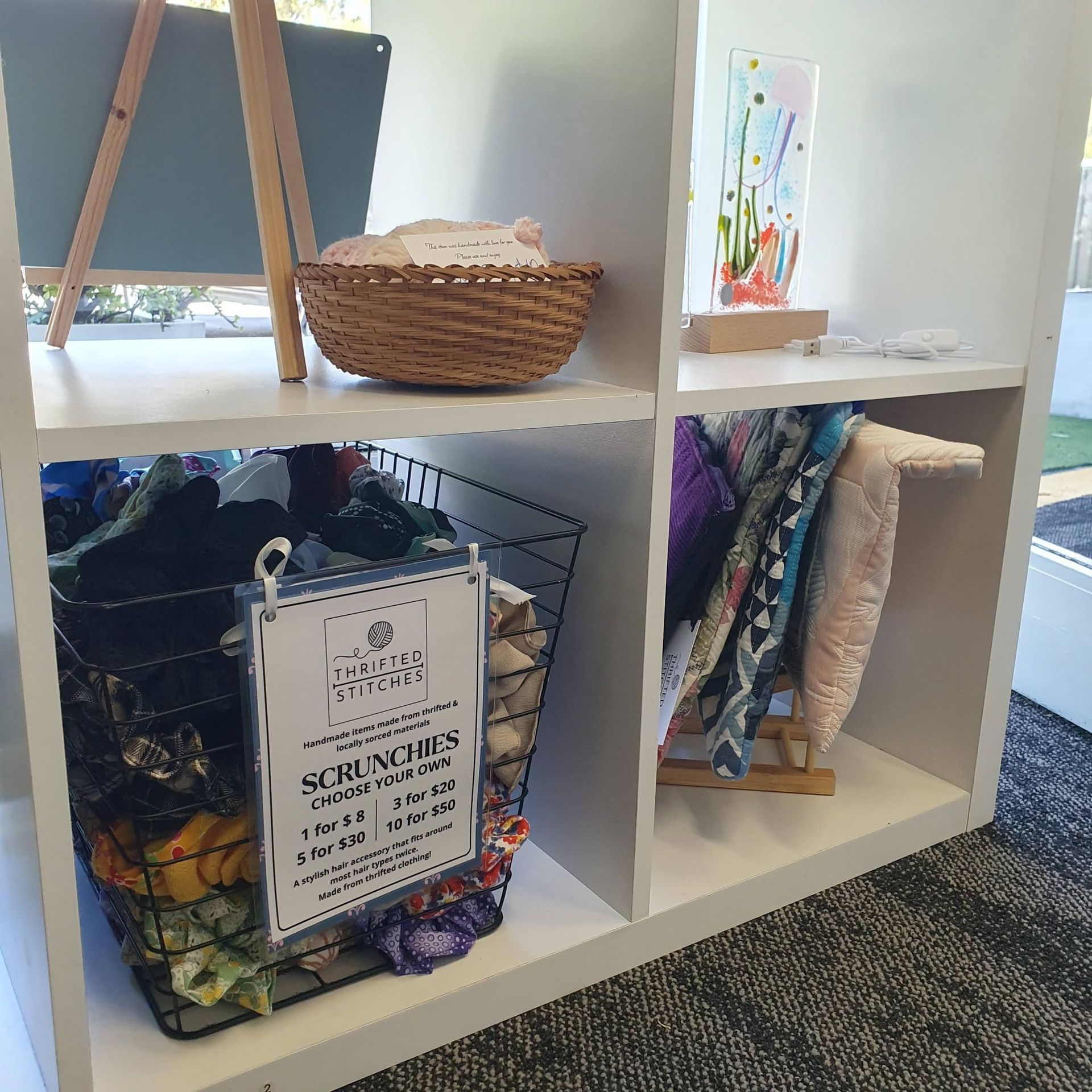 White cubby shelf with baskets, art supplies, and hanging fabric in a bright room. — Tilligerry Collective in Tanilba Bay, NSW