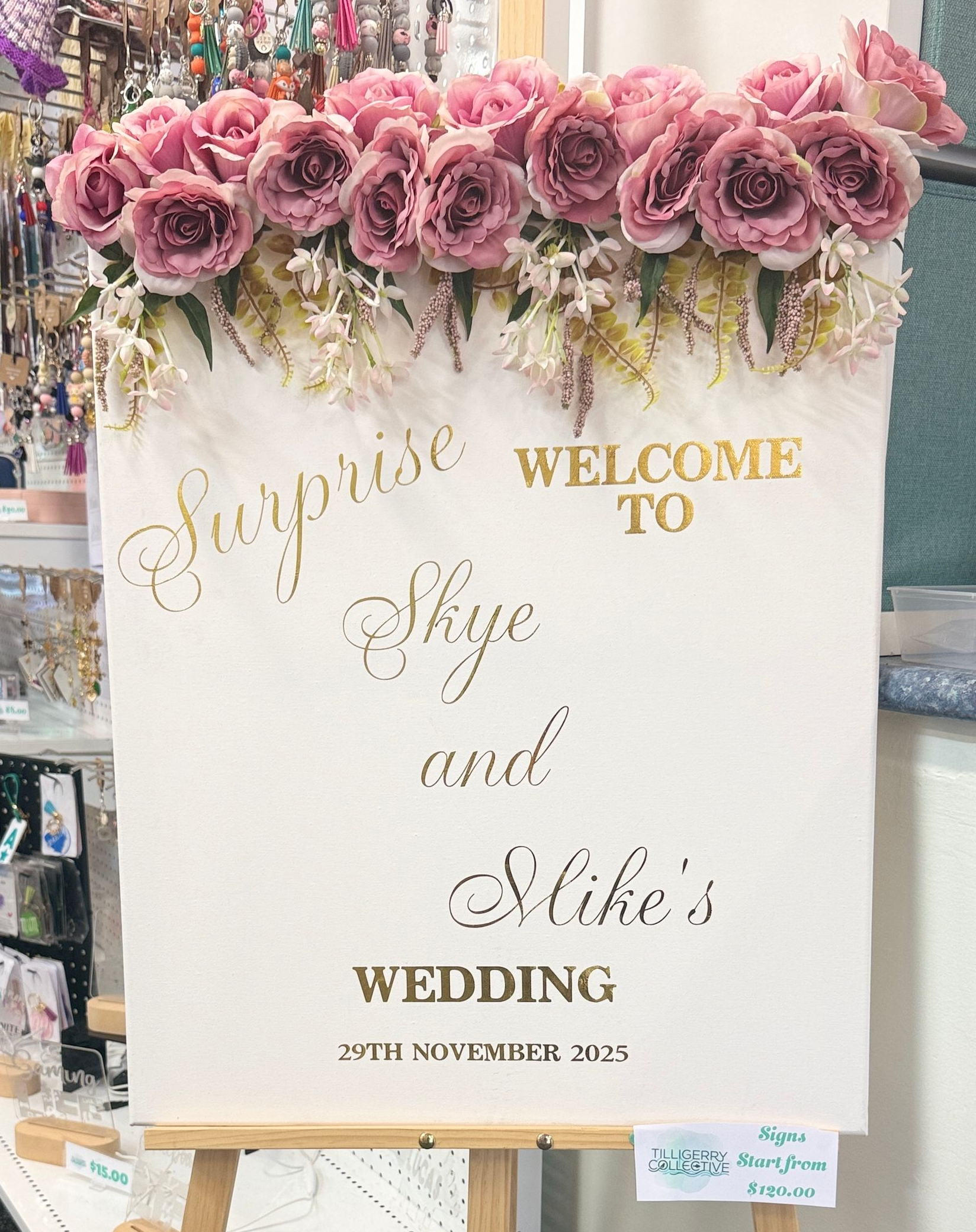 Wedding welcome sign on an easel, decorated with pink flowers and gold lettering in a room. — Tilligerry Collective in Tilligerry Peninsula, NSW