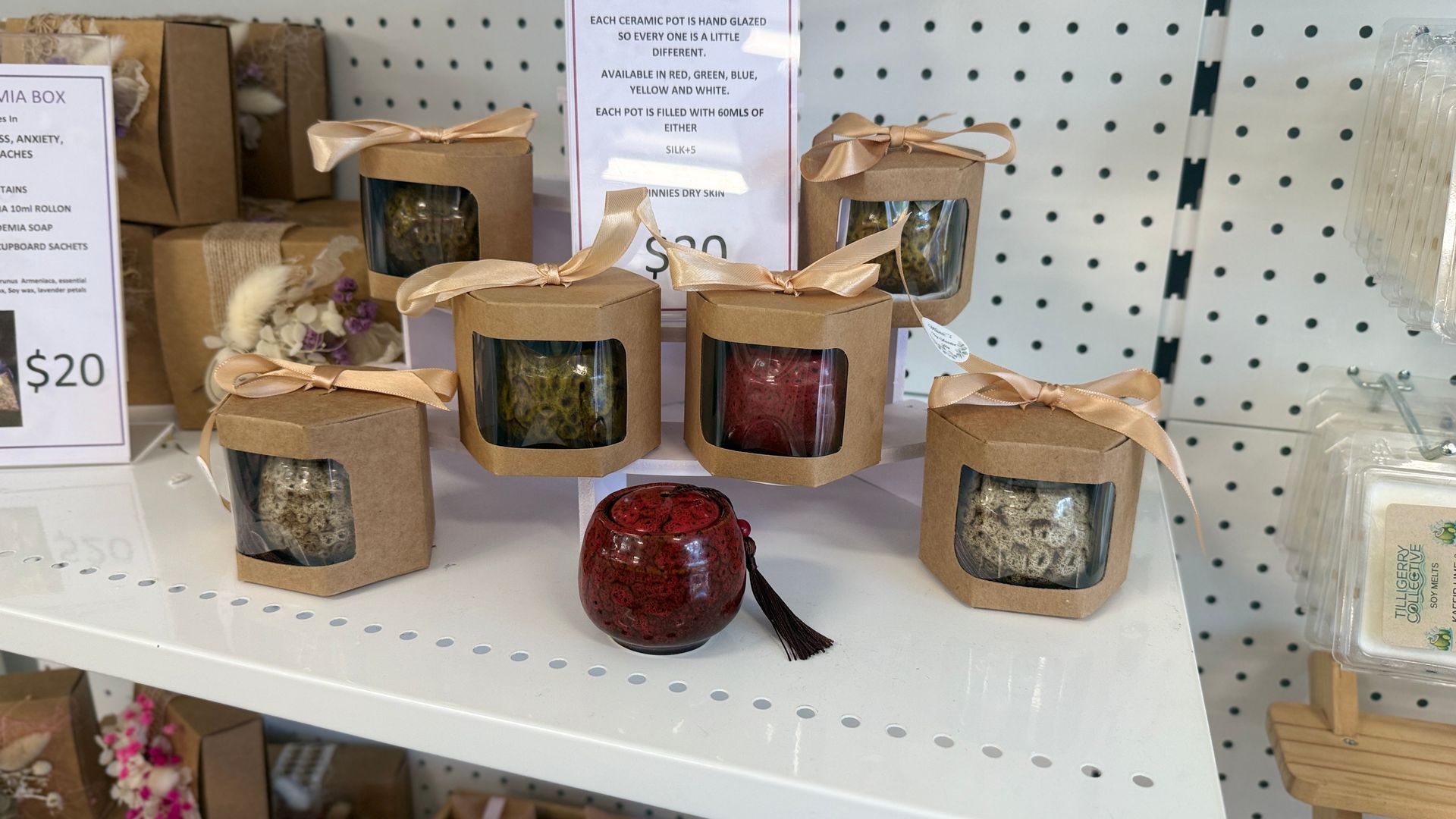 Shelf of wrapped scented candles in kraft paper bags, with a red apple-shaped candle in the center. — Tilligerry Collective in Tilligerry Peninsula, NSW