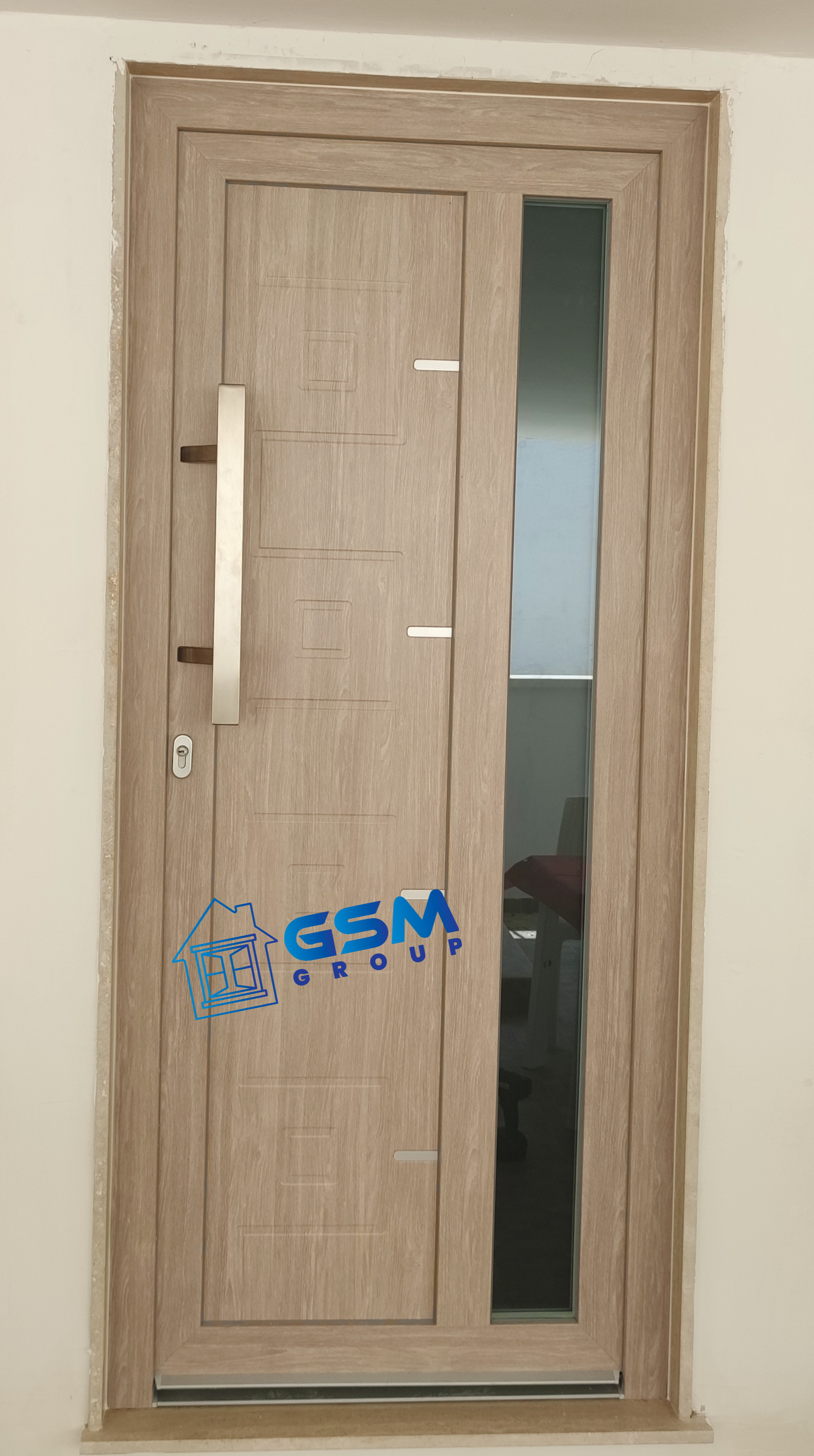 Una moderna porta con finitura effetto legno chiaro, pannello verticale in vetro e lunga maniglia argentata, recante il logo 