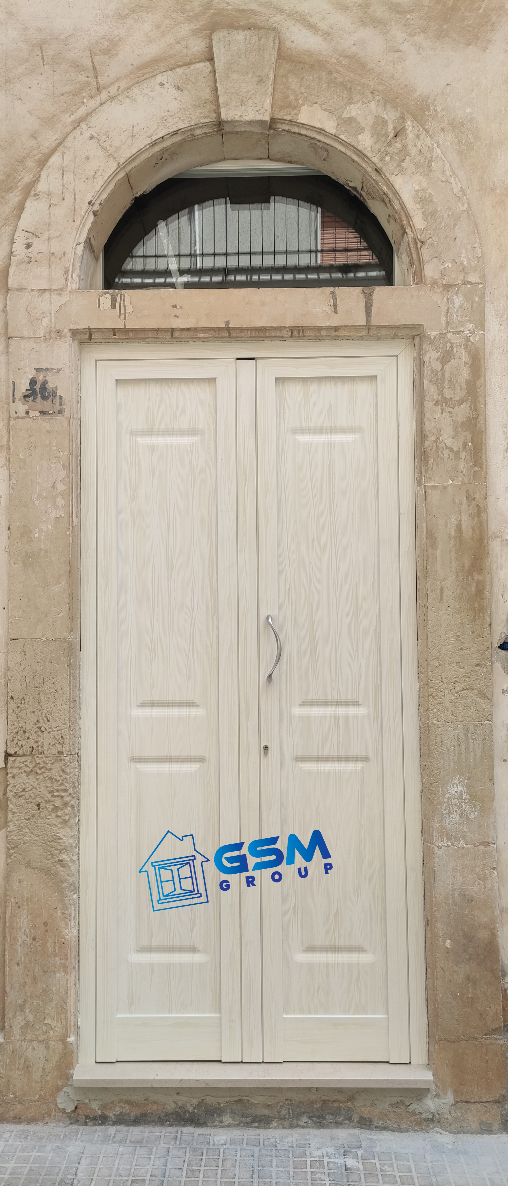 Una porta doppia bianca con sopraluce ad arco semicircolare, inserita in un'antica cornice di pietra.