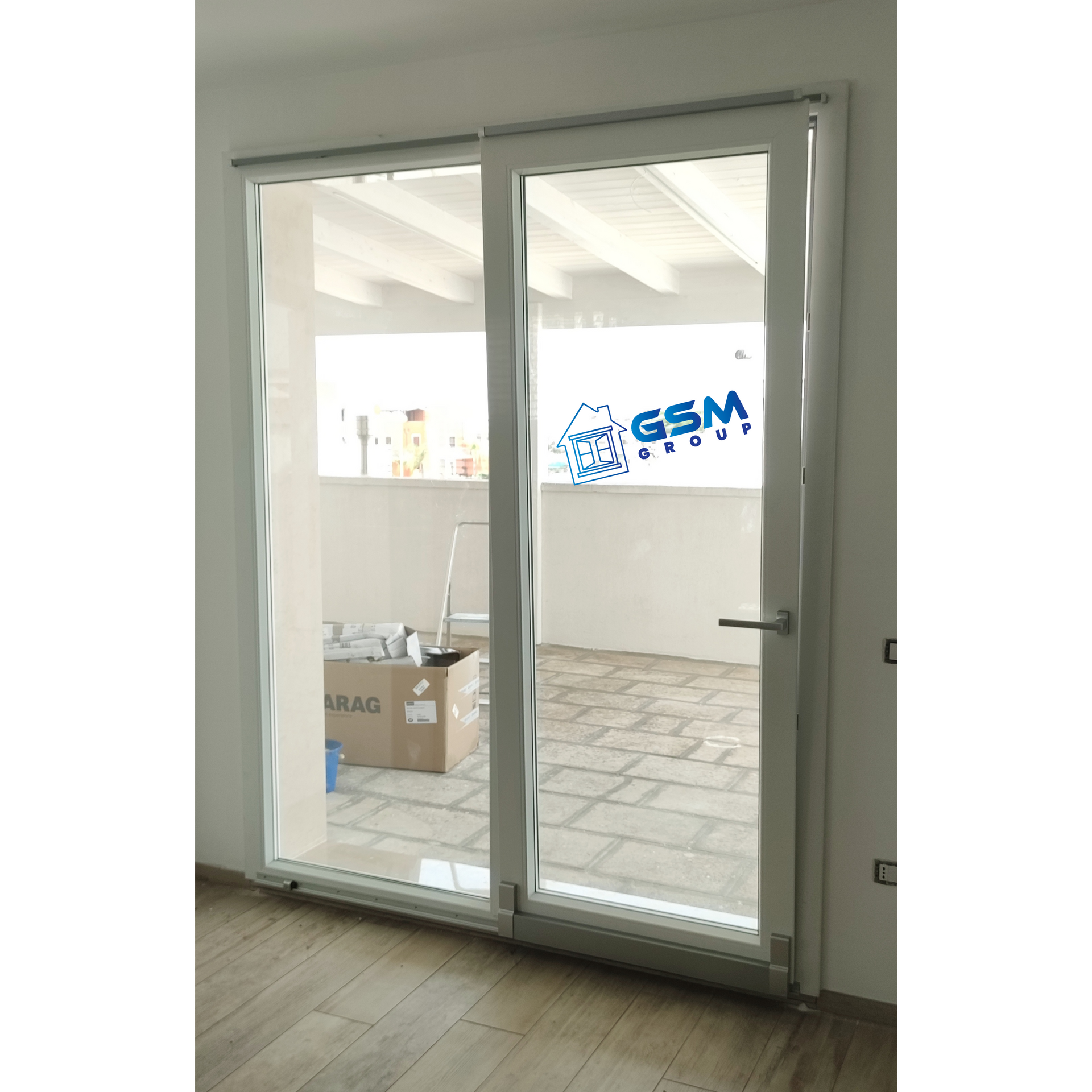 Doppia porta a vetri bianca che si apre su una terrazza piastrellata, con un adesivo con il logo 