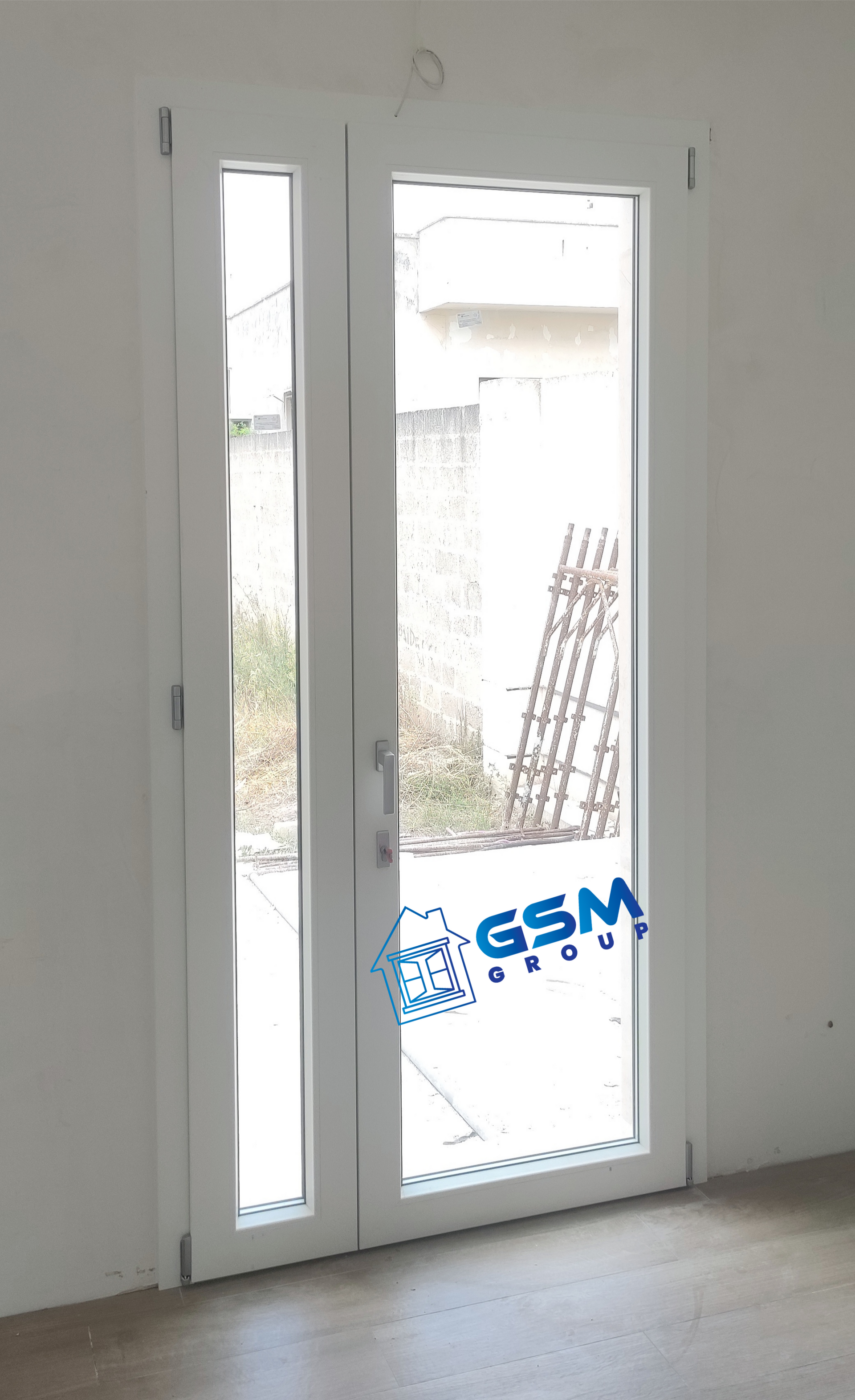 Una porta bianca con un pannello di vetro e una stretta finestra laterale, installata in una stanza semplice e dai colori chiari.