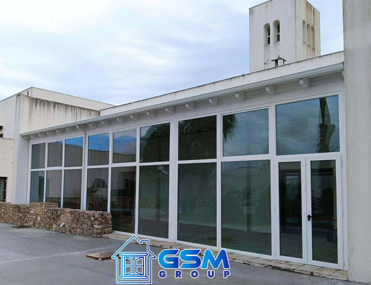 Facciata moderna dell'edificio con pannelli di vetro a tutta altezza e una cornice bianca, su cui spicca il logo del Gruppo GSM nella parte inferiore.