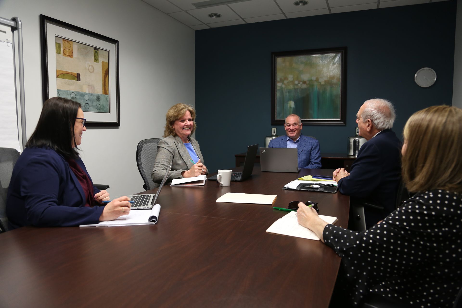 Five people in a conference room around a table, talking during a meeting.