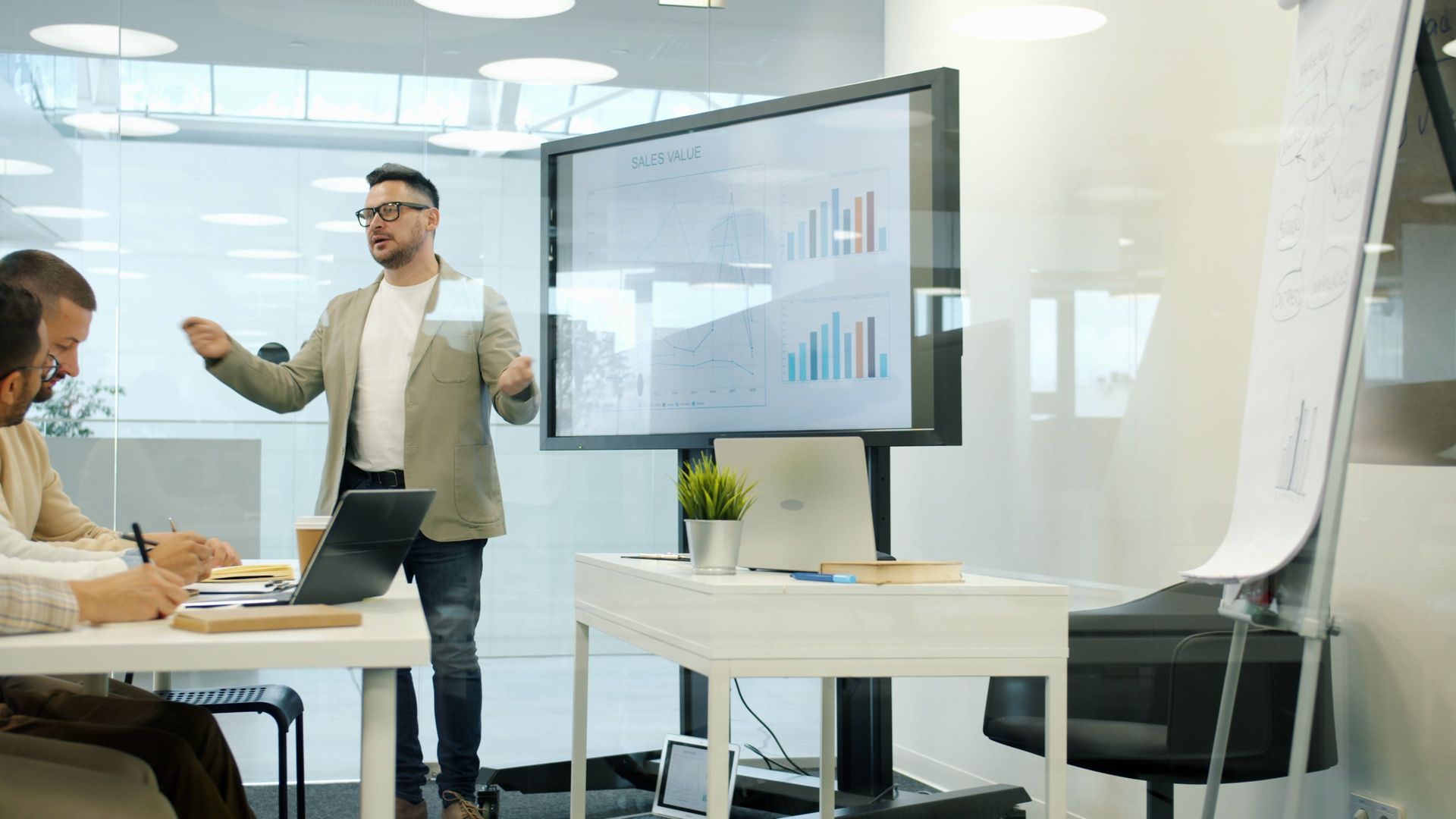 People in a glass-walled conference room discussing a presentation with charts on a screen