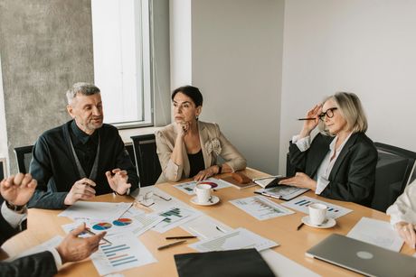 A diverse group of attendees sits in a conference room, listening and looking toward a presentation.
