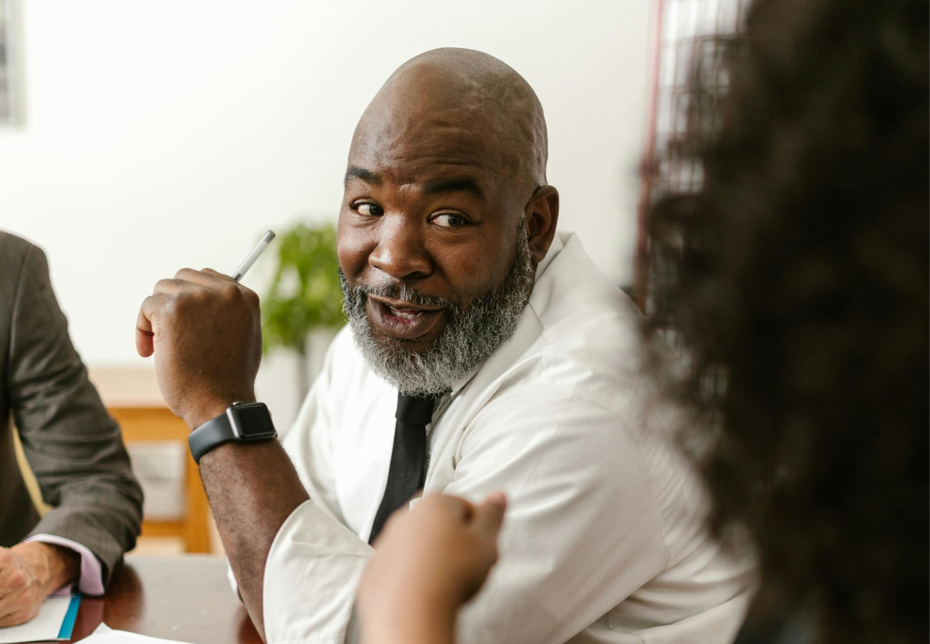 A professional wearing a white shirt and tie gesturing while speaking during a meeting.