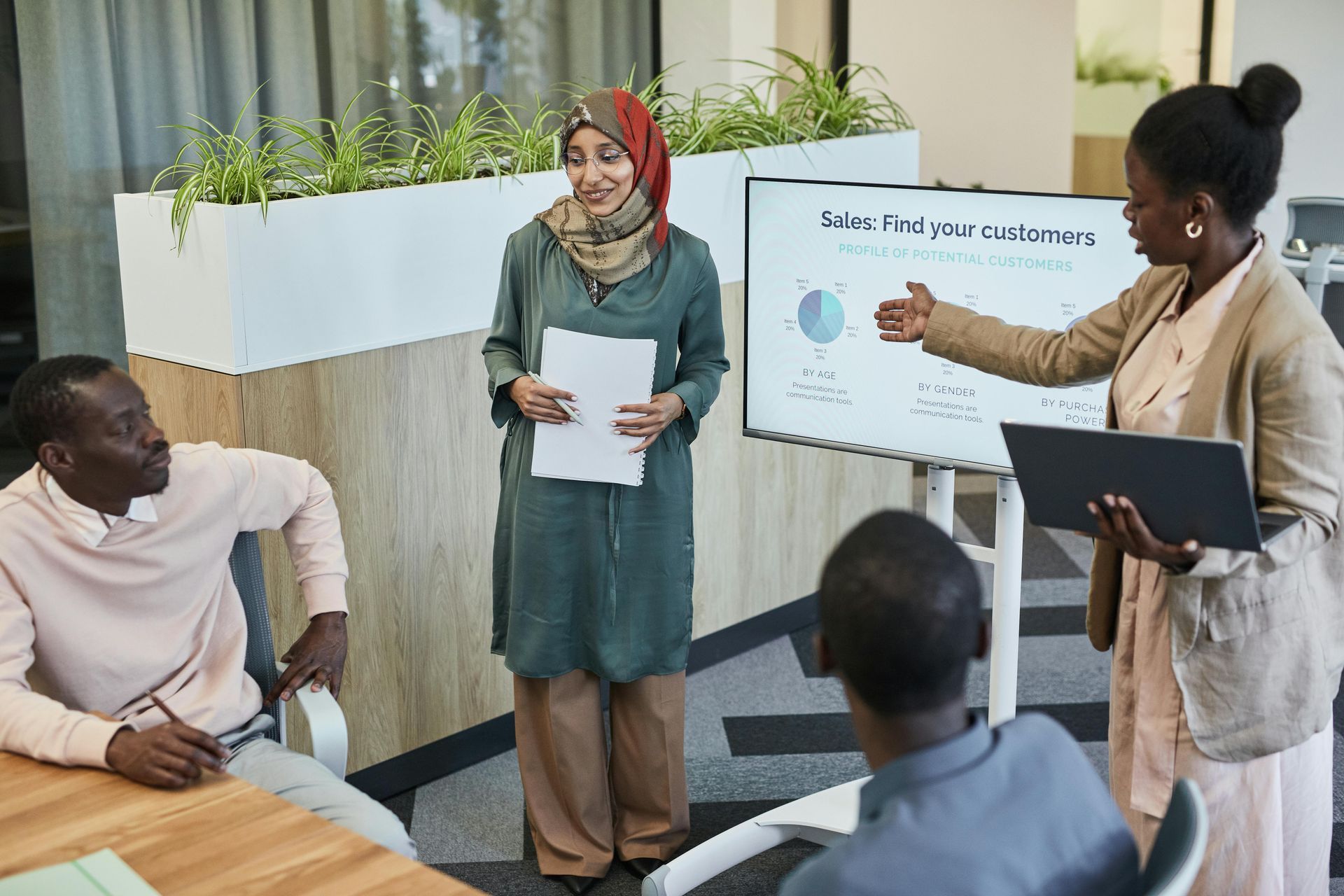 Four people collaborate in a bright office; one person points to a chart on a digital display while another holds notes.