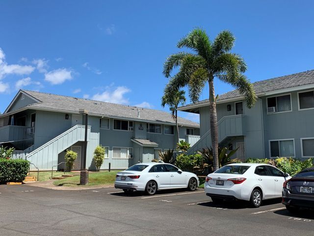 A row of cars are parked in front of a building with palm trees.