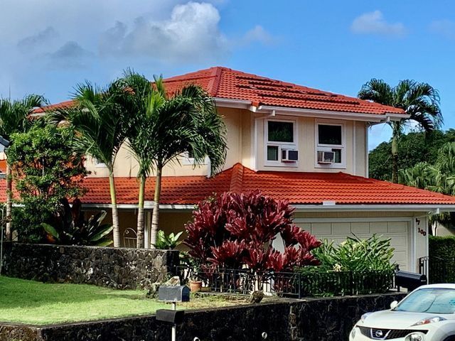 Two-story house with red tile roof, palm trees, and a parked car in the driveway