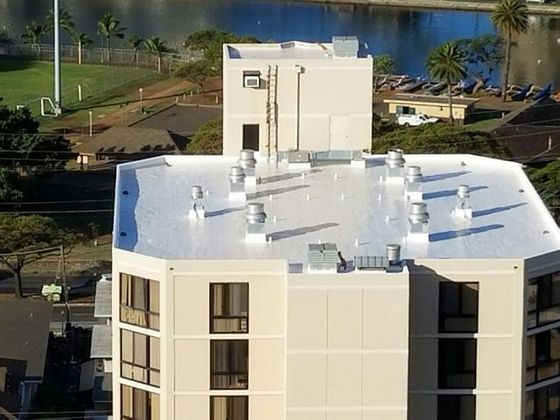 Building rooftop with vents and small tower, overlooking water and greenery.