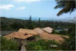 A large house is surrounded by trees and mountains with a view of the ocean.