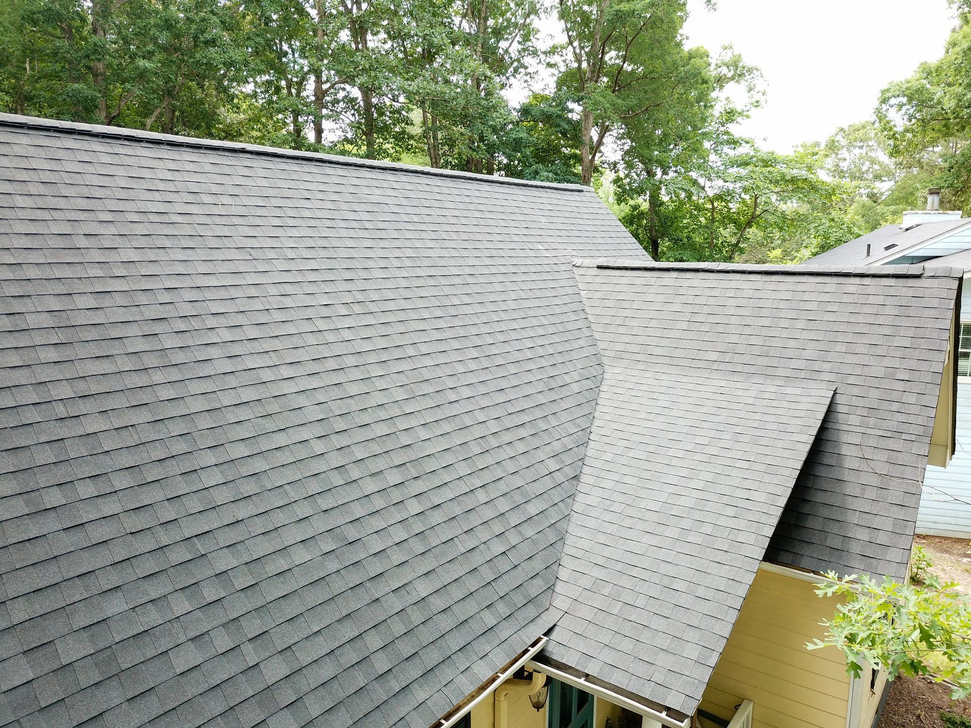 An aerial view of a house with a gray roof and trees in the background.