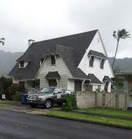 A white house with a black roof and a truck parked in front of it.