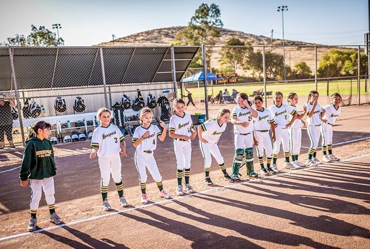 Youth soccer team lined up on a field in white uniforms during a sunny game ceremony