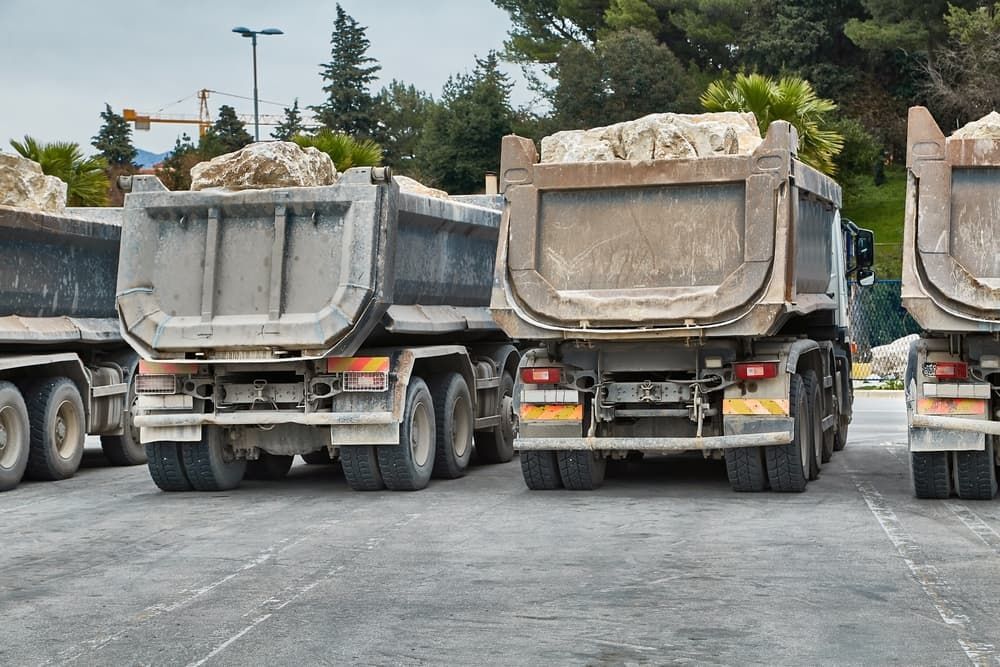 Dump trucks loaded with rocks parked on a paved lot.