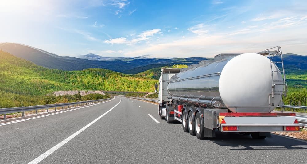Tanker truck driving on a highway with mountains and a blue sky in the background.