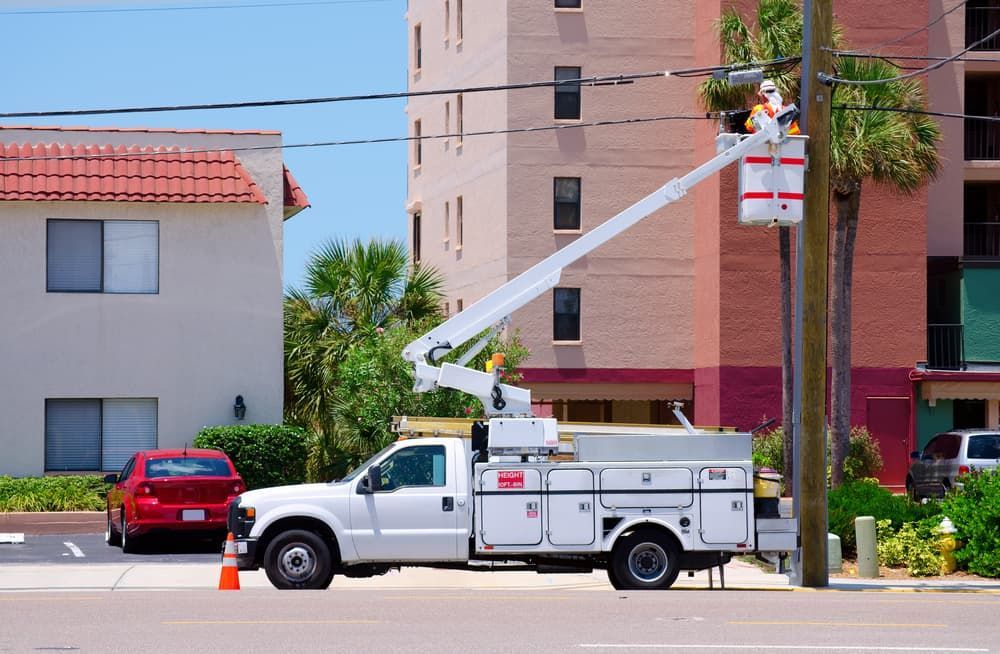 White utility truck with an extended boom, working on power lines near a building.