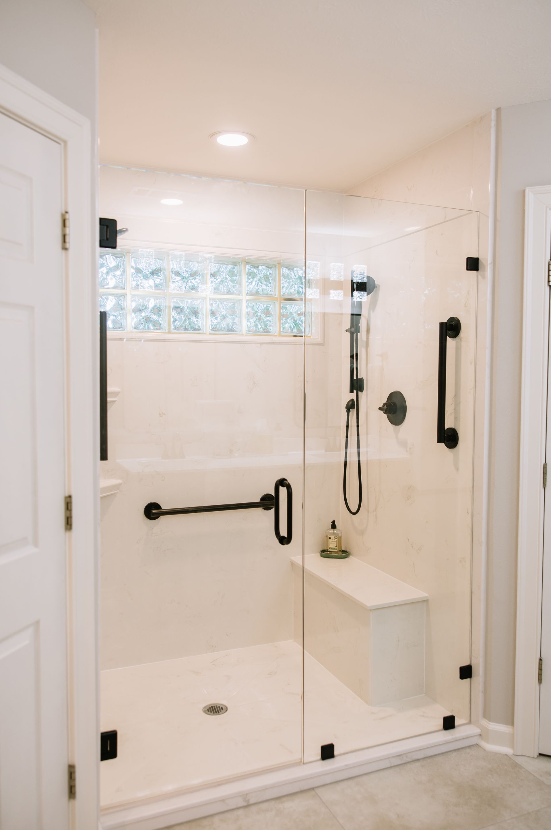 Glass shower with white tile, black hardware, built-in bench, and handheld showerhead
