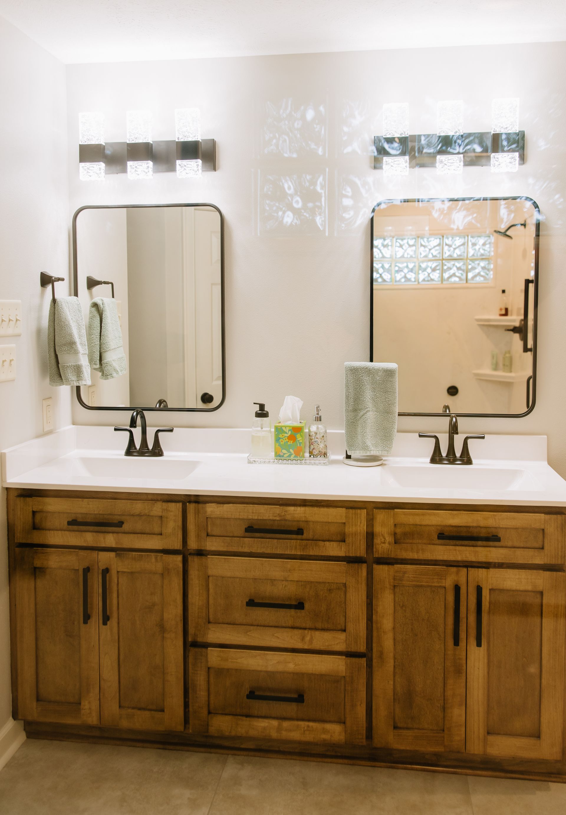 Double vanity bathroom with wood cabinets, two mirrors, sinks, and patterned glass decor